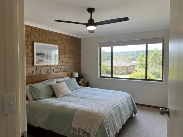 Bedroom with a black ceiling fan above a bed, brick accent wall and window in Erina