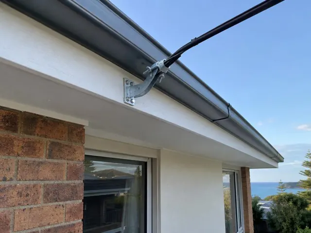 Overhead service cable and point-of-attachment bracket on a brick and rendered house exterior in Forresters Beach