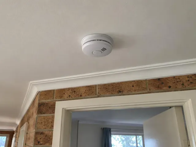 Ceiling-mounted smoke alarm above a doorway in a brick and plaster home in Terrigal